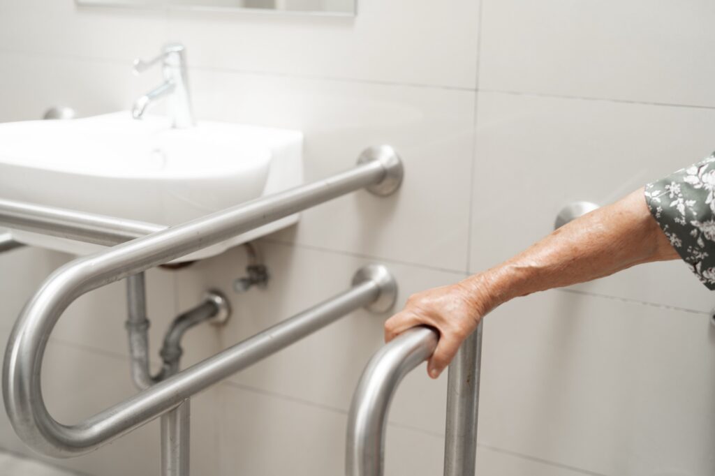 Older adult holding a stainless steel grab bar beside the toilet and sink