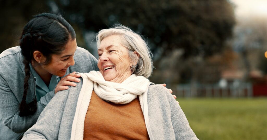 Caregiver smiling with a senior woman in a wheelchair outdoors